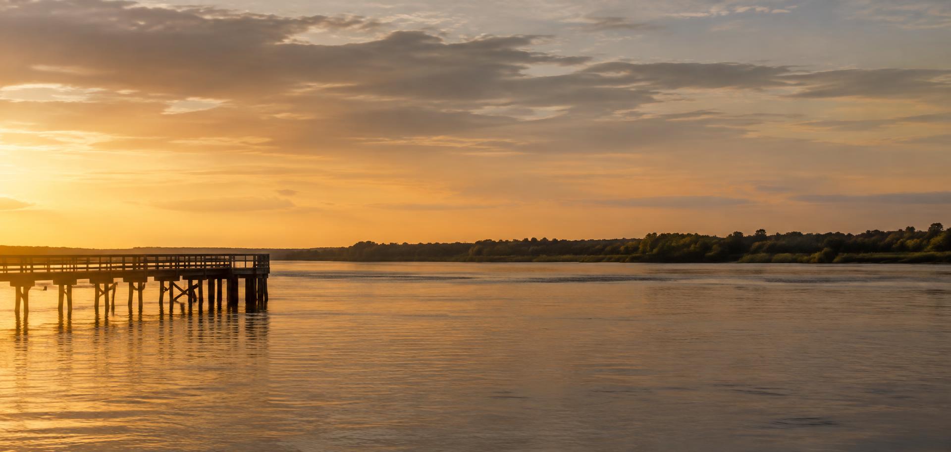 A broad calm river at golden hour with a wooden pier